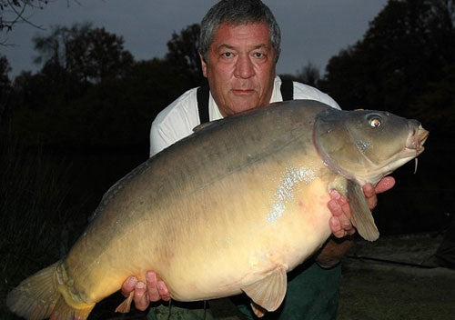 Ken holding a large carp in front of him, in dim outdoor lighting.