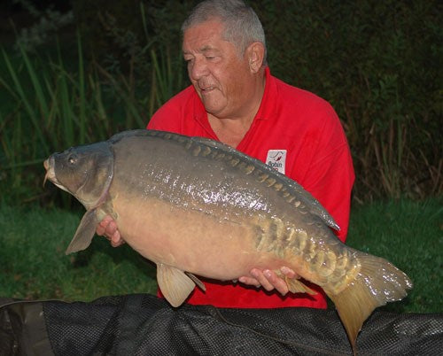 Ken holding a have carp fish and looking down at it.