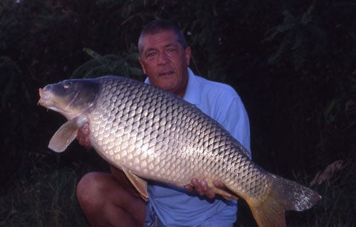 Ken holding a carp in dim outer lighting.