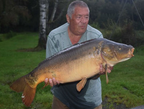 Ken holding a huge open-mouthed carp in dim lighting.