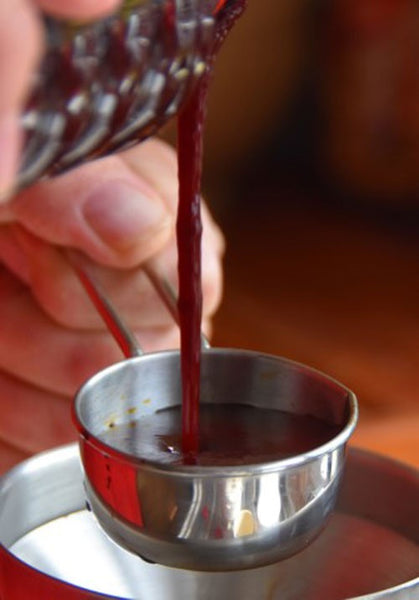 Hand pouring Haith's Liquid Robin Red into silver measuring spoon.