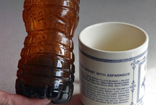 Bottle filled with brown liquid next to a mug.