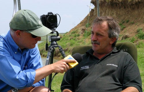A man holding a microphone to another man, with a black filming camera in the background.