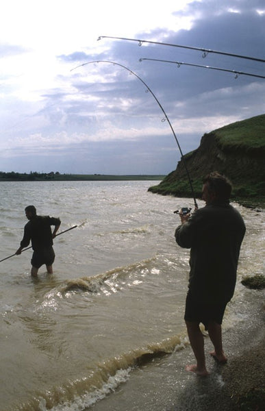 Two men in water, holding rods.