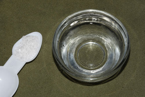 a measured 3g spoon of Betaine HCL crystals and a small bowl containing 15ml of tap water