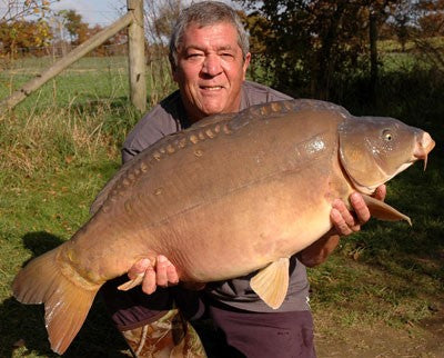 Image of Ken Townley holding a large carp by the lakeside