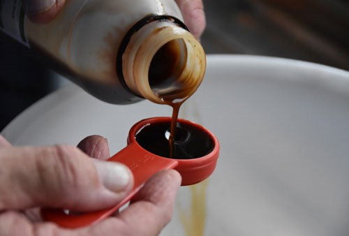 Photo of white plastic bowl with liquid attractor being poured into it with a red measuring spoon