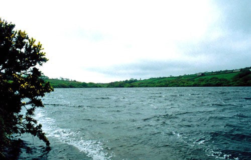 Photo of a fishing lake with a green hillside behind it
