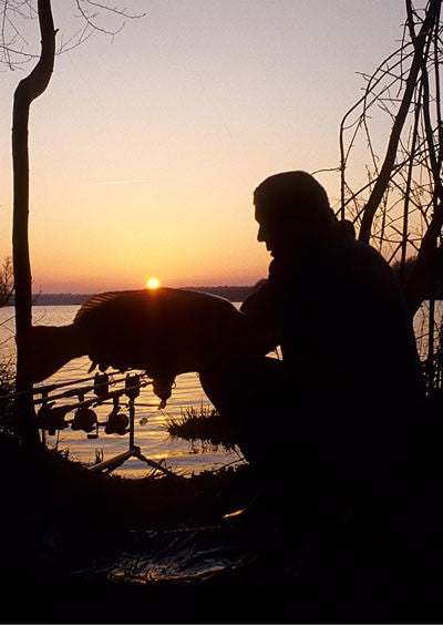 Image of Ken Townley at sunset by a lakeside holding a carp