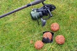 Image of a fishing rod with four balls of groundbait on the grass