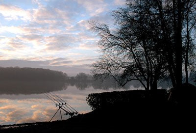 Image of a lake with fishing rods, misty trees at the front of the lake