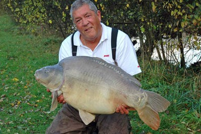 Image of Ken Townley holding a large carp on the pond side.