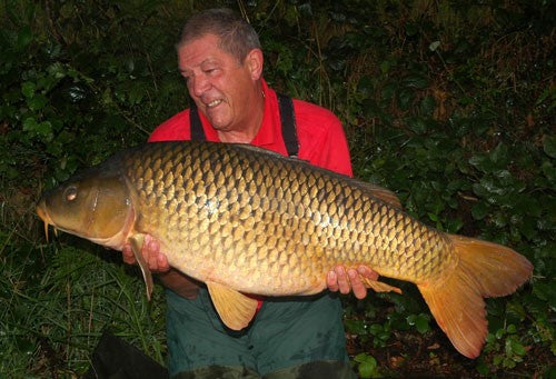 Photo of Ken Townley holding a large carp at night time beside a lake