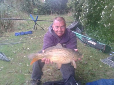 Photo of man at the pond side holding a large carp