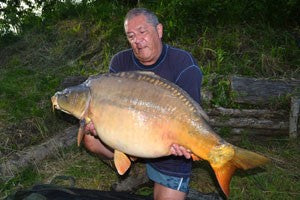 Photo of Ken Townley holding a large carp at the river bank