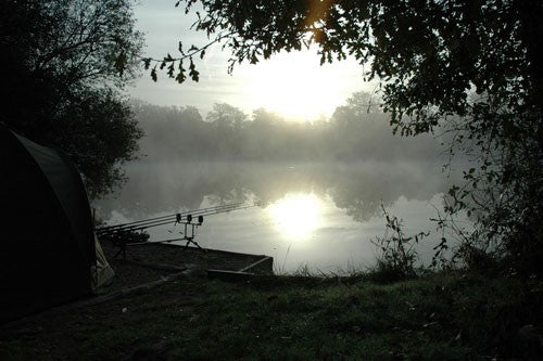 Photograph of a fishing lake at dusk with a tent and fishing rods