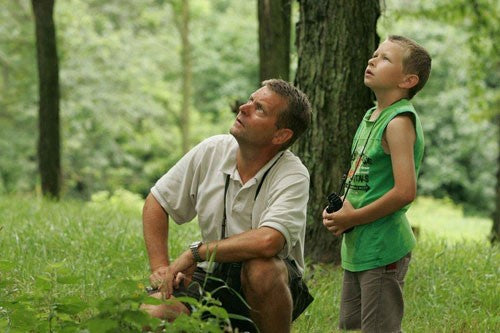 Image of a man kneeling down next to a young boy both birdwatching with binoculars