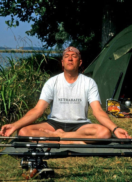 Photo of Ken Townley sat on the grass with his legs croseed and his eyes closed in a yoga position.