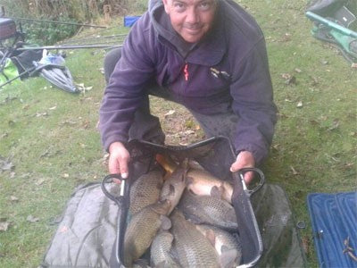 Photo of man at lakeside holding a basket full of carp
