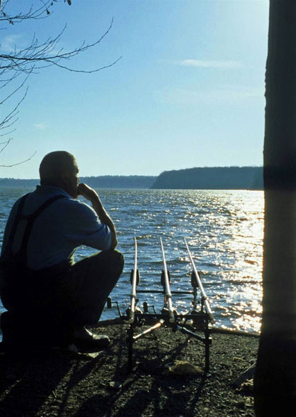 Photo of Ken Townley sat beside a lake looking out onto the water next to his fishing rods