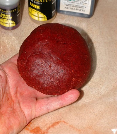 Photo of large red round boilie being held in the palm of hand