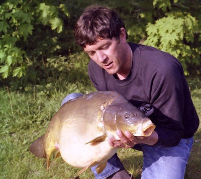 Image of a fisherman knelt down holding a large carp