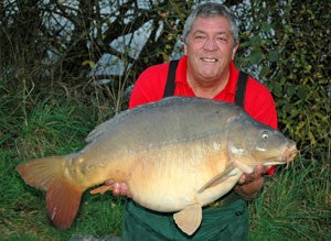 Photo of Ken Townley holding a large carp in front of some bushes
