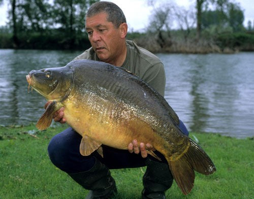 Photo of Ken Townley holding a large carp by the side of a pond