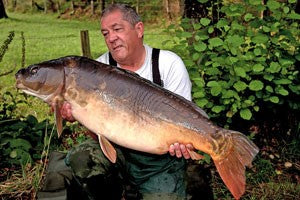 Photo of Ken Townley wearing a white shirt holding a large carp by the side of a pond