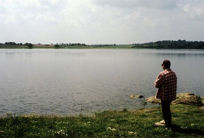 Image of a fisherman stood on the lakeside overlooking the water