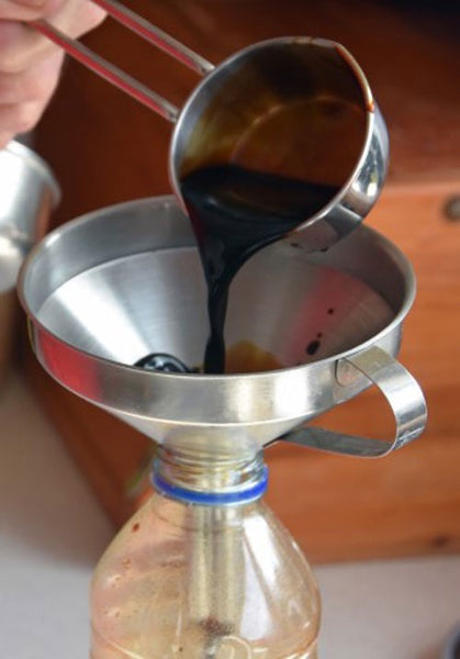Dark brown soy sauce being poured through a metal funnel.