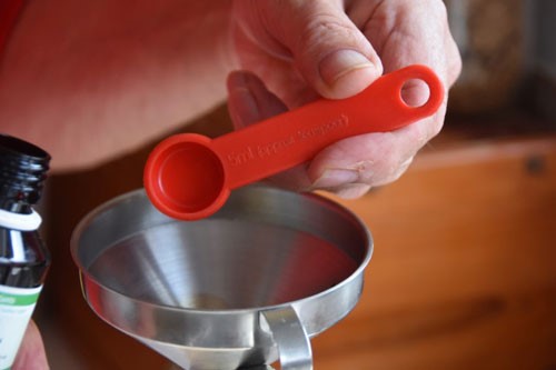 Hand holding a small red measuring spoon.
