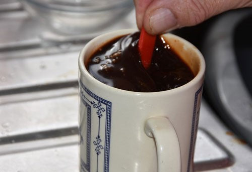 Sticky fishing liquids being stirred by a red spoon in a mug.