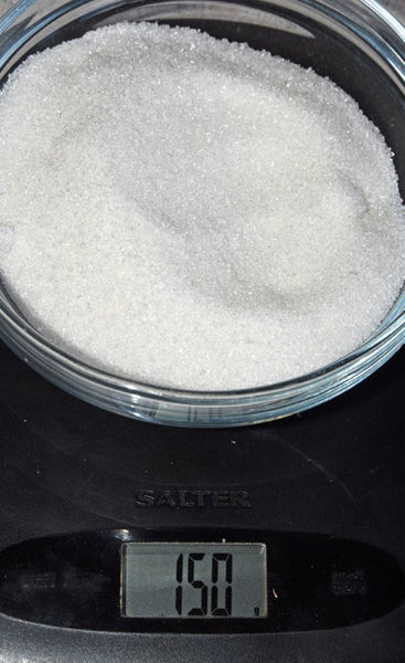 150g of white granulated sugar on a pair of scales.