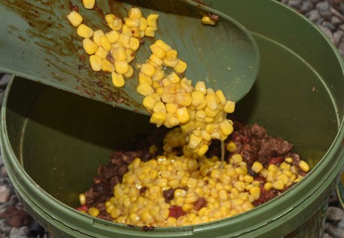 Sweetcorn being transferred to a green bucket and mixed with red boilies.