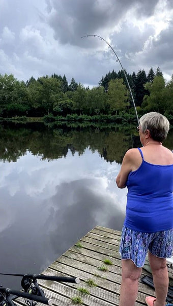 Tat holding a fishing line into a still lake.