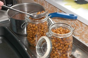 Someone transferring tiger nuts into hot glass jam jars.