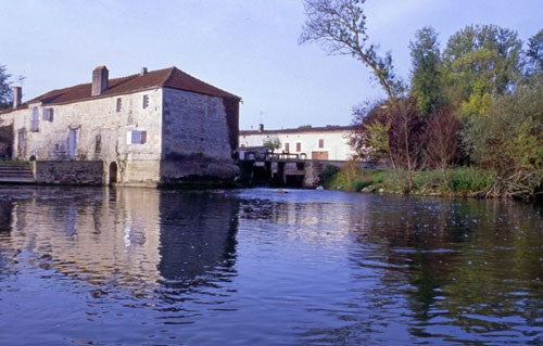 Old watermill next to open water and greenery.