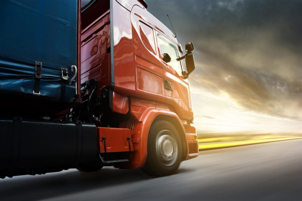 red and black truck driving towards a storm at dusk