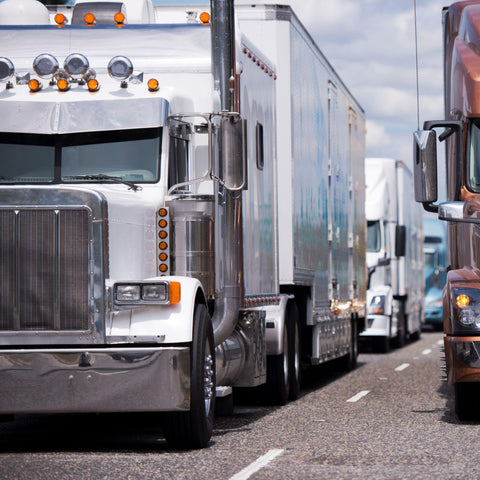 Convoy of big rigs semi trucks with semi trailers running on the highway in several lines