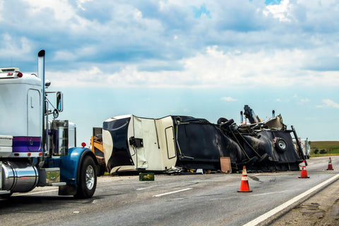 Fifth wheel RV overturned on highway with wench truck trying to get it off the road and two semis parked nearby and traffic cones keeping traffic away