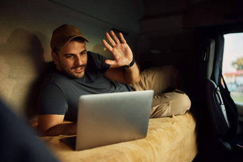 Happy driver making video call over laptop while relaxing in truck cabin.