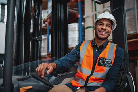 Happy forklift driver sitting in vehicle in warehouse