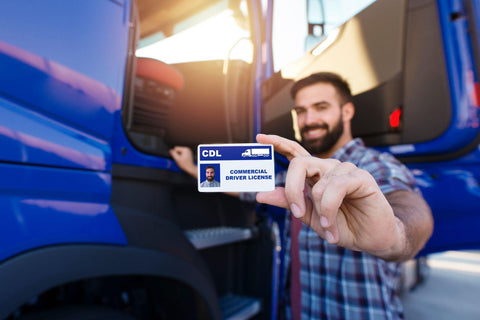 Middle aged truck driver standing by his truck and showing his commercial driver license. Focus on CDL license.