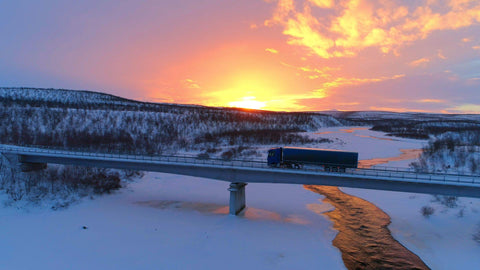 Semi truck crossing the bridge above icy river in the winter at sunset