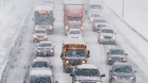 Several vehicles are traveling slowly down a multi lane road on an icy stormy day.