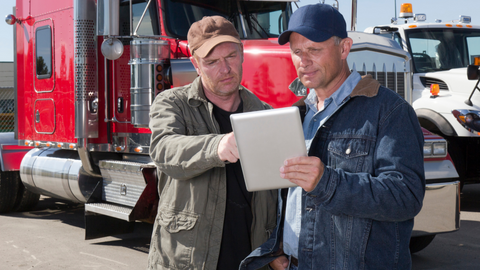 Two truck drivers using a tablet PC in front of trailers.