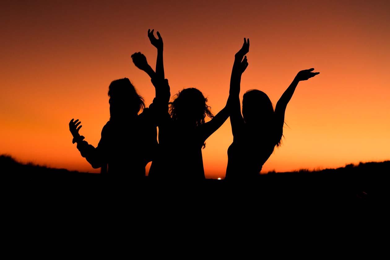 silhouette of three women happily dancing at sunset