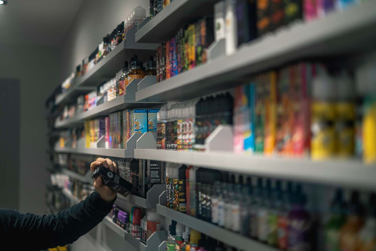 man wearing a black long-sleeved shirt selecting a vape from a shelf