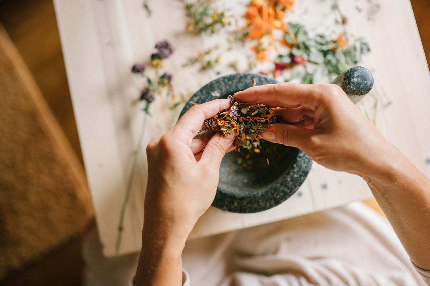 Person holding dried herbs over a mortar and pestle